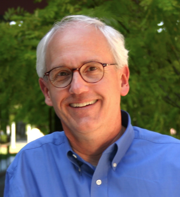 Headshot of Dr. Yock - man with glasses and a button down shirt in front of a bush