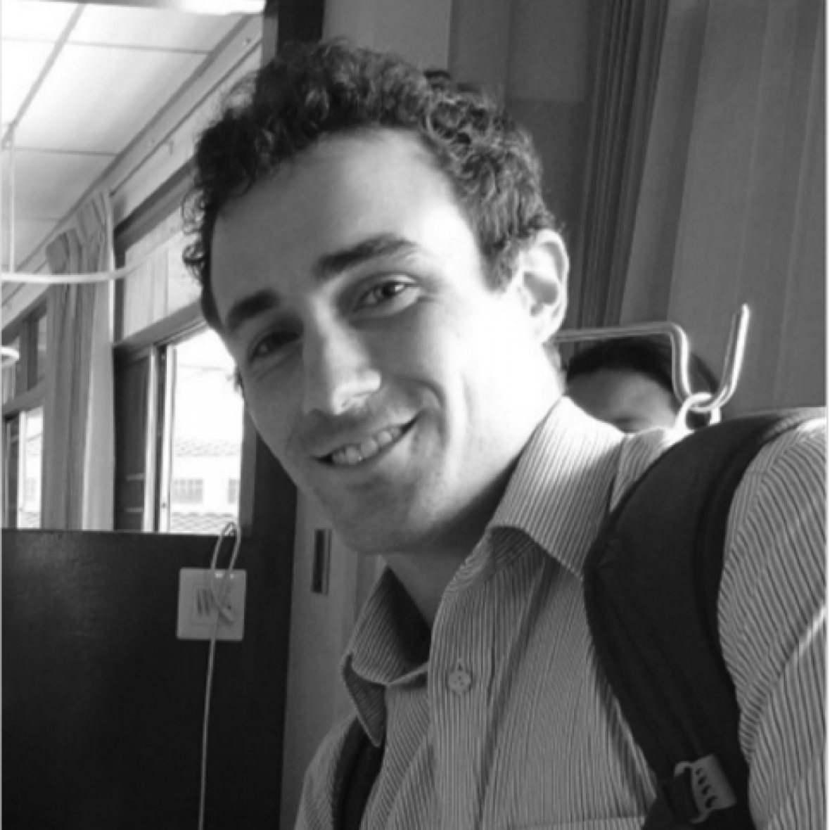 Watson Fellow smiles at camera, wearing a button-down shirt and backpack, in black and white