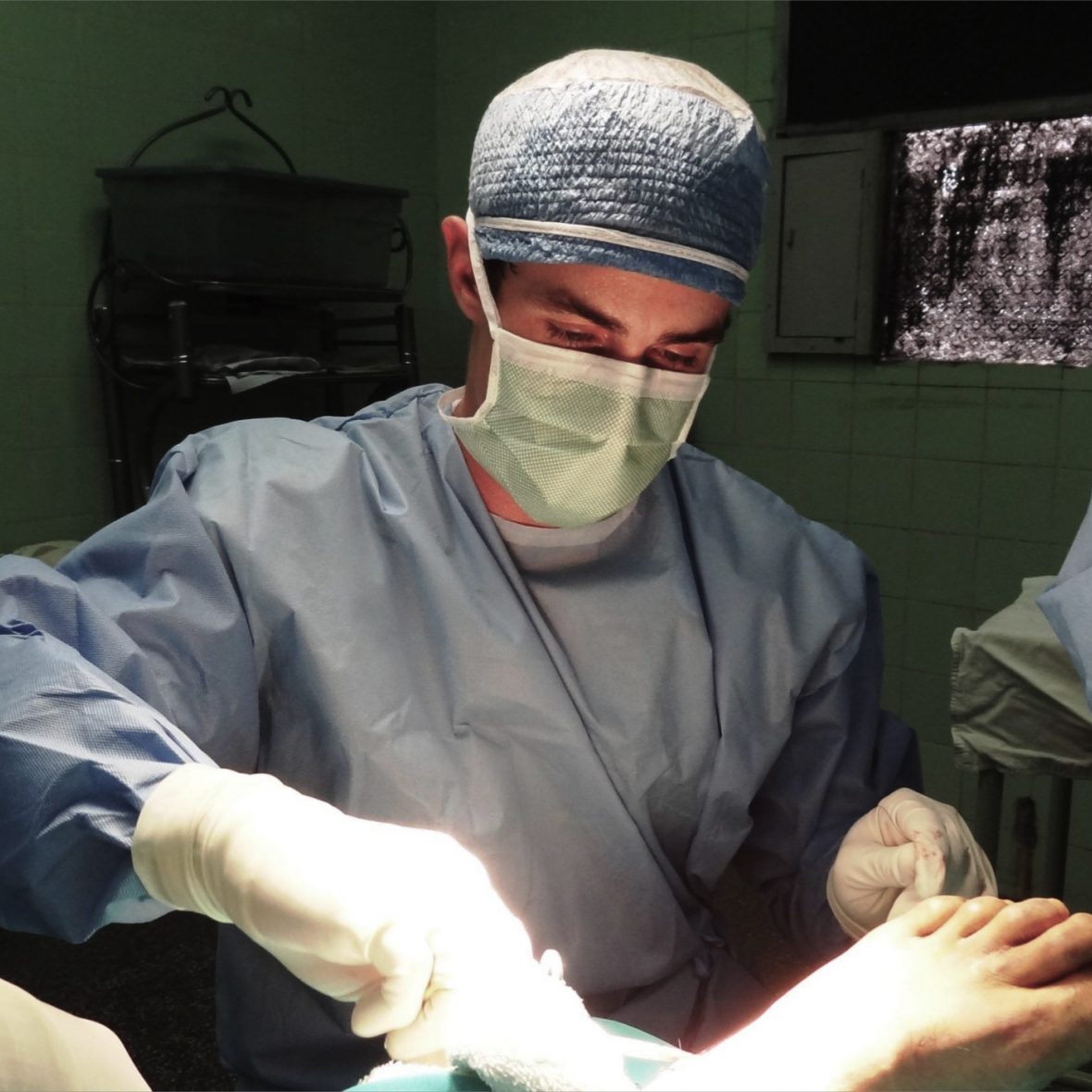 photo of Watson Fellow performing surgery, wearing light blue scrubs, headlamp attached, white gloves on arms